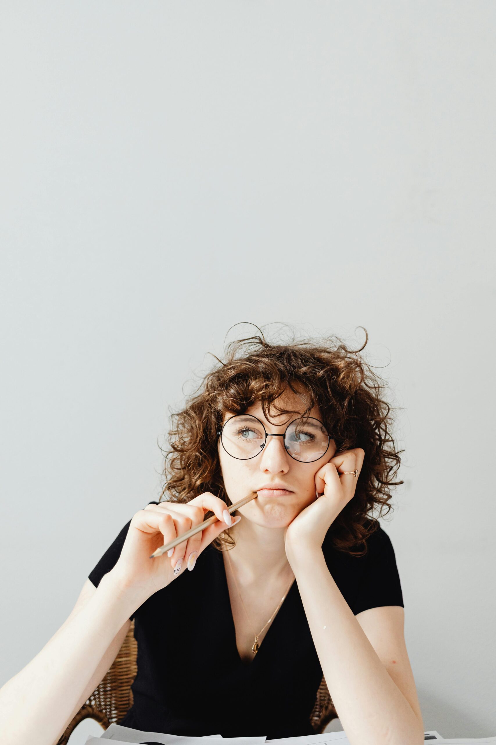 Caucasian woman with curly hair and glasses in a thoughtful pose indoors.